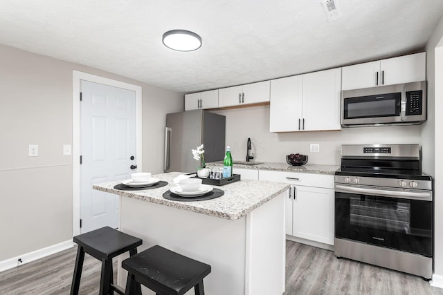 kitchen with light hardwood / wood-style floors, white cabinetry, a textured ceiling, and appliances with stainless steel finishes