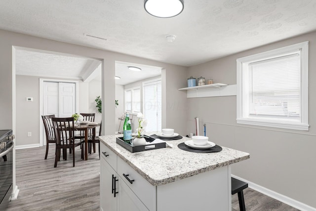 kitchen featuring white cabinetry, light stone counters, wood-type flooring, a textured ceiling, and stainless steel stove