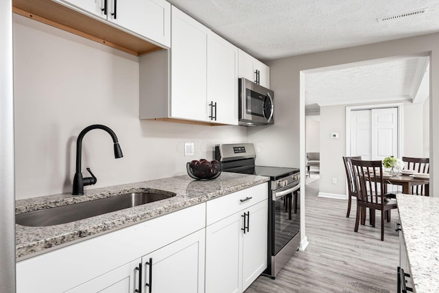 2789 Berrell Ave, Columbus, OH 43211 - kitchen featuring appliances with stainless steel finishes, white cabinetry, light stone counters, a textured ceiling, and light wood-style floors