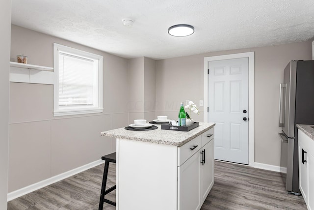 kitchen with white cabinets, a center island, stainless steel fridge, and hardwood / wood-style flooring