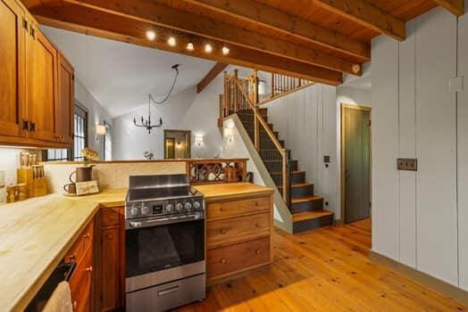 kitchen with lofted ceiling with beams, light hardwood / wood-style flooring, stainless steel gas stove, kitchen peninsula, and a chandelier