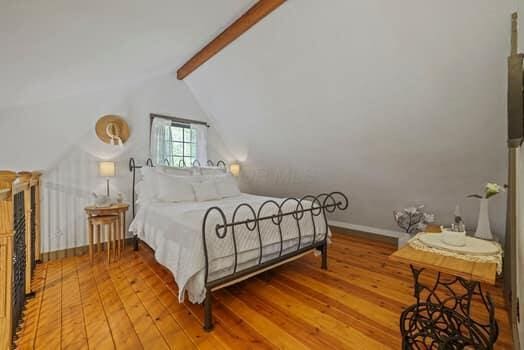 bedroom with lofted ceiling with beams and light wood-type flooring