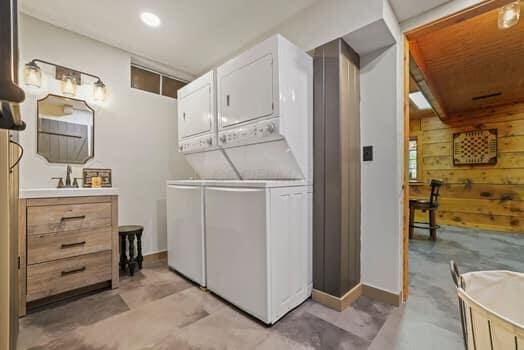 clothes washing area with stacked washer / dryer, wooden walls, and sink