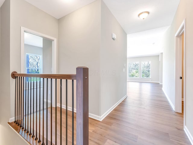 corridor with baseboards, wood finished floors, and an upstairs landing