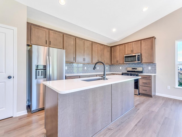 kitchen with vaulted ceiling, tasteful backsplash, a sink, light wood finished floors, and appliances with stainless steel finishes