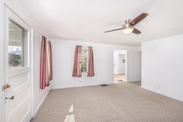 empty room with ceiling fan, a healthy amount of sunlight, and light carpet