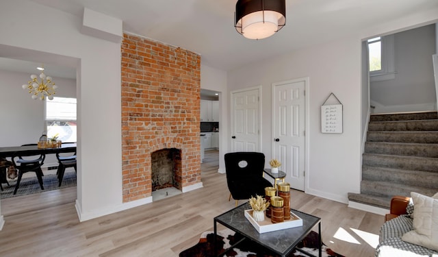 living room with a brick fireplace, a wealth of natural light, a chandelier, and light wood-type flooring