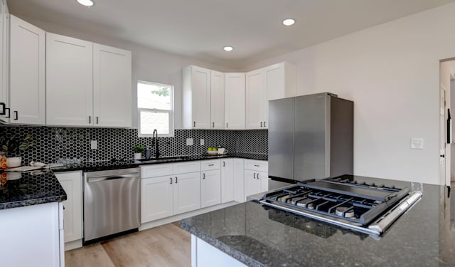 kitchen with white cabinets, sink, light hardwood / wood-style flooring, dark stone countertops, and stainless steel appliances