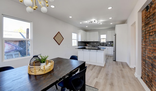 dining space with plenty of natural light, an inviting chandelier, brick wall, and light hardwood / wood-style flooring