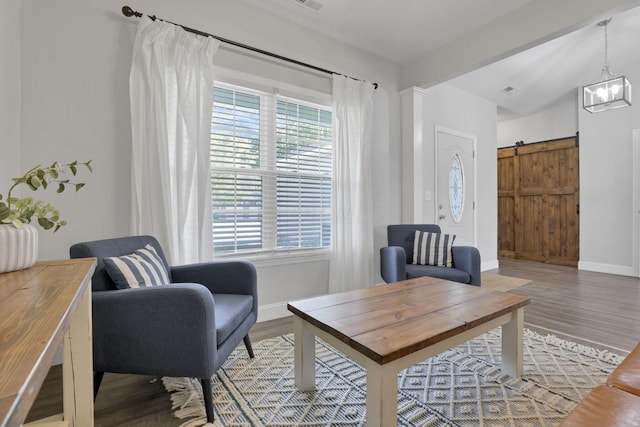 living area featuring beam ceiling, a barn door, hardwood / wood-style floors, and a notable chandelier