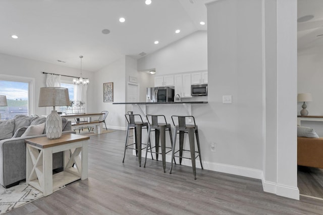 kitchen with white cabinetry, stainless steel appliances, kitchen peninsula, hardwood / wood-style floors, and a kitchen bar