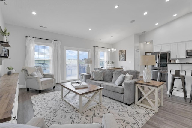 living room with a chandelier, high vaulted ceiling, light hardwood / wood-style flooring, and plenty of natural light