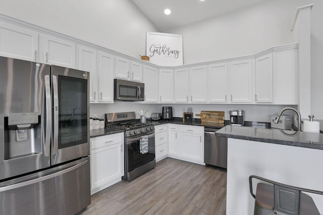 kitchen featuring stainless steel appliances, light hardwood / wood-style flooring, high vaulted ceiling, dark stone countertops, and white cabinetry