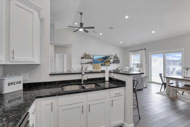 kitchen featuring dark stone counters, sink, vaulted ceiling, a kitchen bar, and white cabinetry