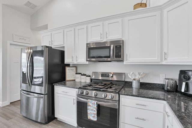 kitchen featuring dark stone counters, white cabinetry, light hardwood / wood-style floors, and appliances with stainless steel finishes