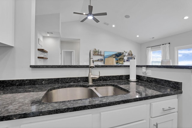 kitchen with dark stone counters, ceiling fan, sink, white cabinets, and lofted ceiling