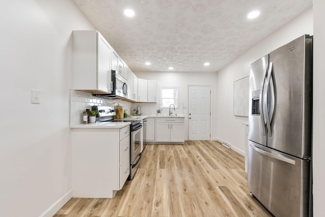 kitchen with white cabinetry, decorative backsplash, light hardwood / wood-style flooring, and stainless steel appliances