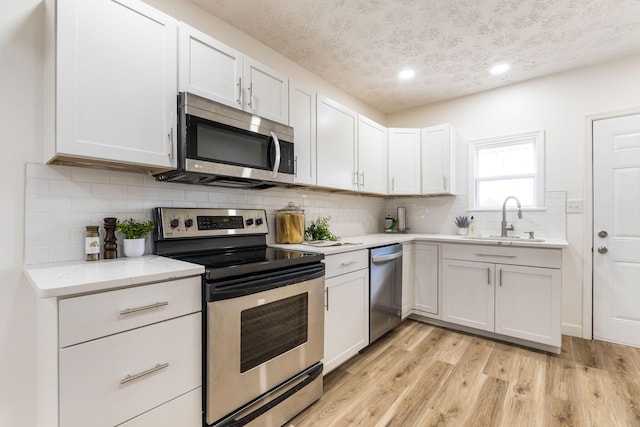 kitchen featuring white cabinetry, sink, light hardwood / wood-style floors, and appliances with stainless steel finishes