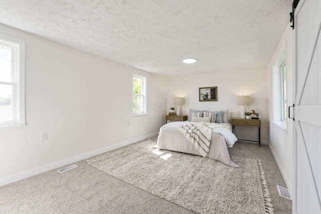 carpeted bedroom featuring a barn door and a textured ceiling