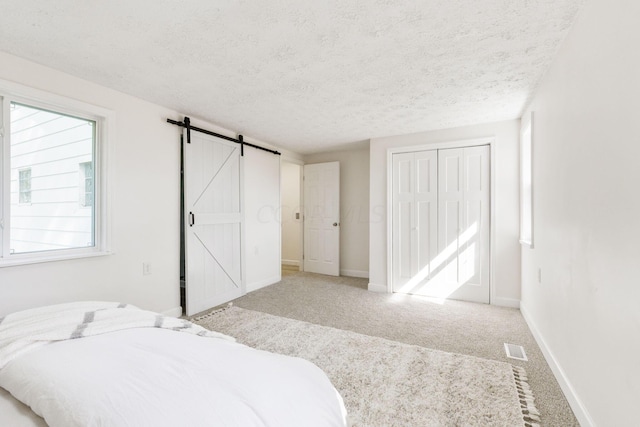 bedroom with a closet, a barn door, light carpet, and a textured ceiling