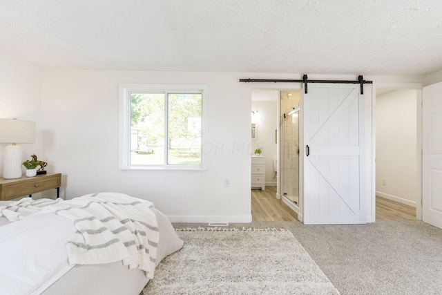 carpeted bedroom with connected bathroom, a barn door, and a textured ceiling