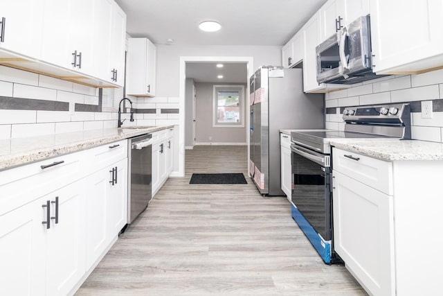 kitchen featuring light stone countertops, appliances with stainless steel finishes, light wood-type flooring, sink, and white cabinetry