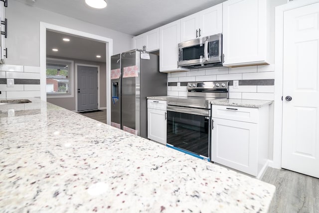 kitchen featuring white cabinets, light stone counters, stainless steel appliances, and light hardwood / wood-style flooring