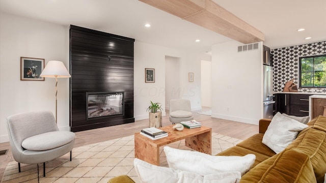 living room featuring beamed ceiling, a large fireplace, and light hardwood / wood-style flooring