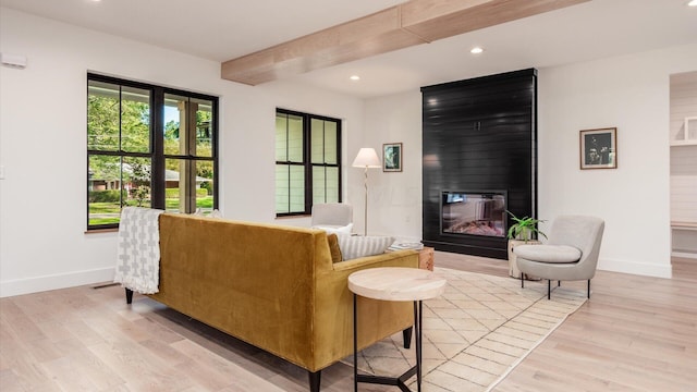 living room featuring a large fireplace, beamed ceiling, and light hardwood / wood-style floors