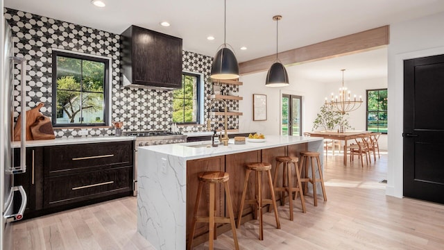 kitchen with a center island with sink, extractor fan, a notable chandelier, and light wood-type flooring