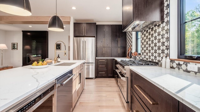 kitchen featuring pendant lighting, backsplash, wall chimney range hood, light stone counters, and stainless steel appliances