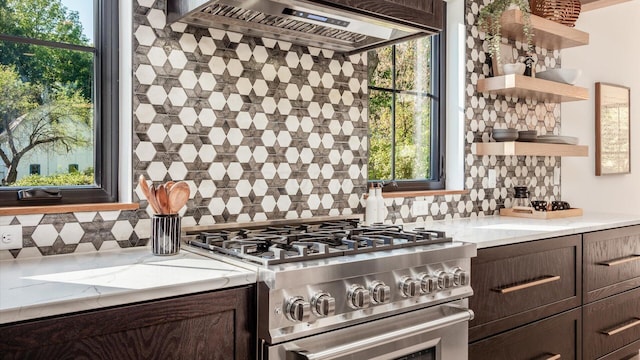 kitchen with backsplash, wall chimney range hood, high end stainless steel range oven, dark brown cabinets, and light stone counters