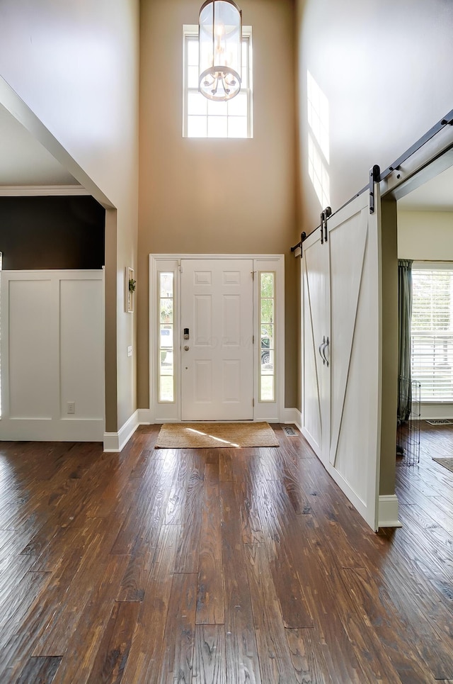 entryway with plenty of natural light, a barn door, a towering ceiling, and dark wood-type flooring