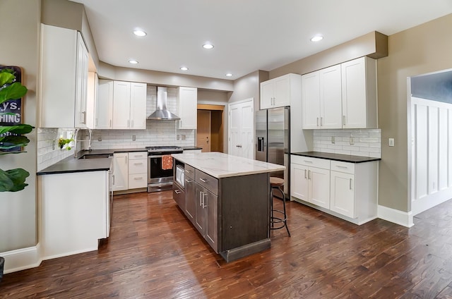 kitchen with wall chimney exhaust hood, white cabinets, a kitchen island, and stainless steel appliances