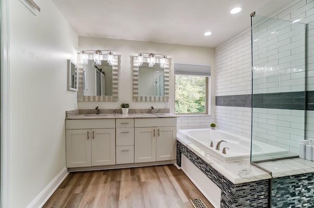 bathroom featuring hardwood / wood-style floors, a relaxing tiled tub, and vanity