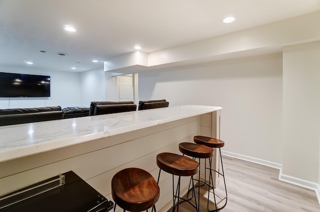 kitchen featuring a kitchen bar, light hardwood / wood-style floors, and light stone counters