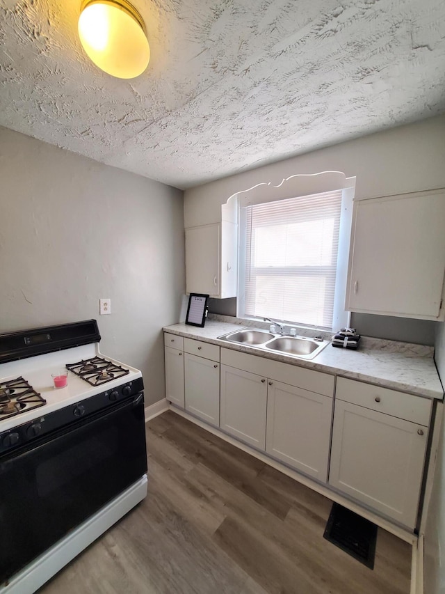 kitchen with sink, white gas range, a textured ceiling, dark hardwood / wood-style flooring, and white cabinetry