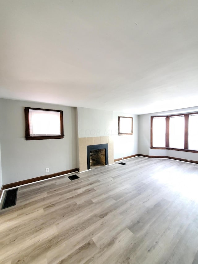 unfurnished living room featuring a healthy amount of sunlight, light wood-type flooring, and a tiled fireplace