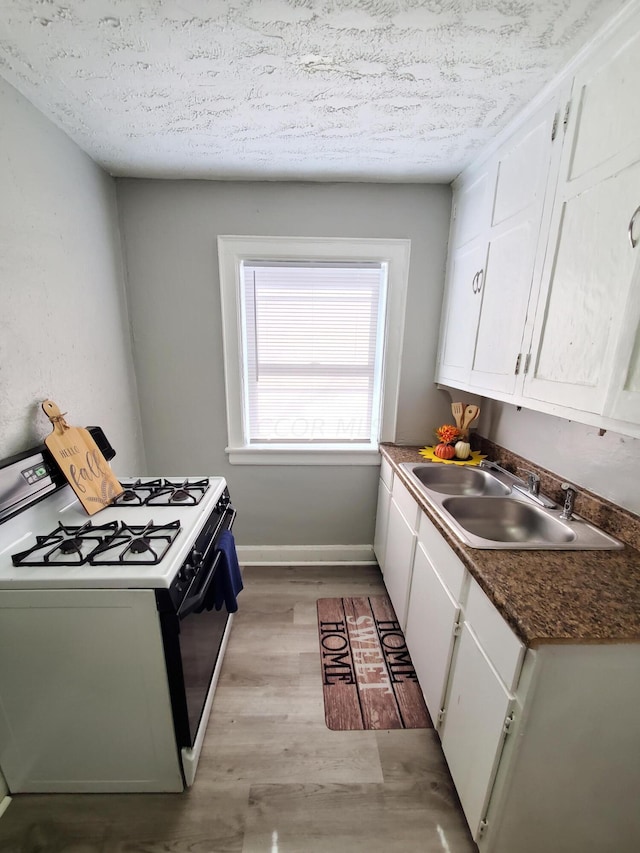 kitchen with white cabinets, sink, light wood-type flooring, a textured ceiling, and gas stove