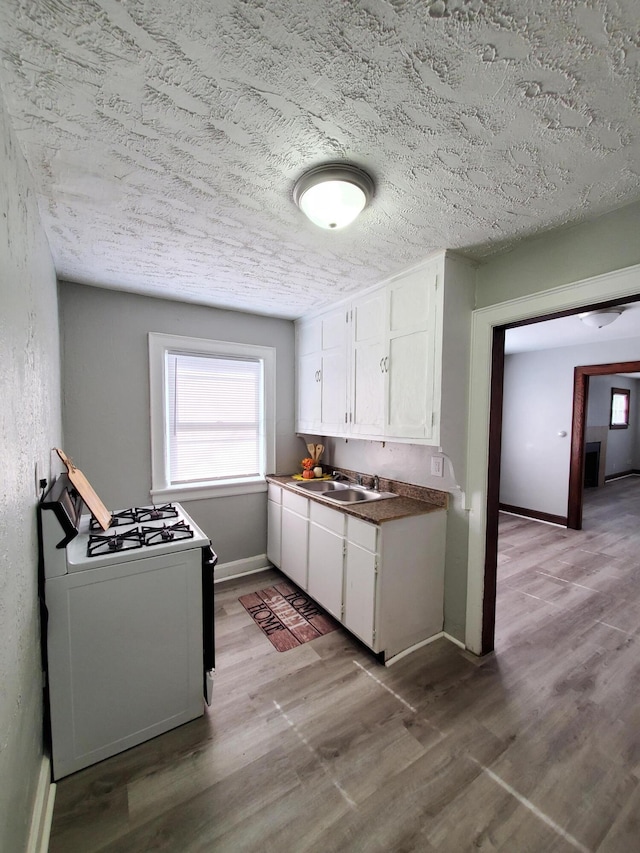 kitchen with light wood-type flooring, a textured ceiling, sink, white cabinets, and white stove