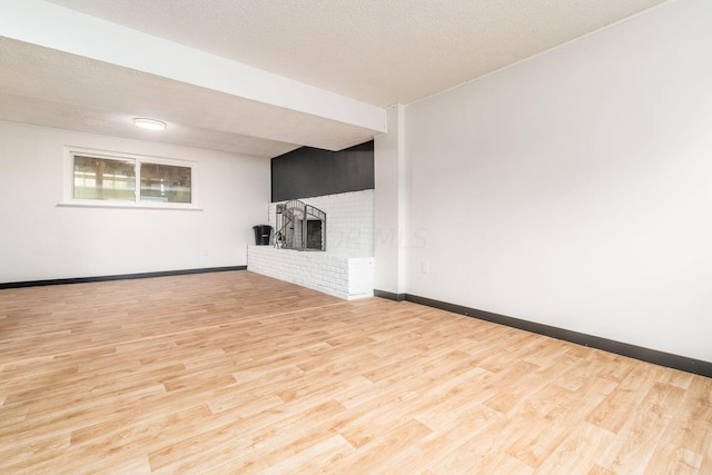 unfurnished living room featuring a brick fireplace, a textured ceiling, and light hardwood / wood-style flooring