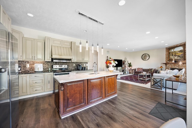 kitchen with cream cabinets, dark hardwood / wood-style flooring, hanging light fixtures, and an island with sink