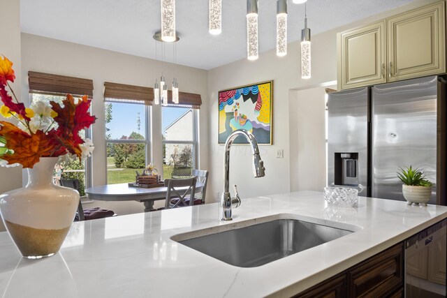 kitchen featuring stainless steel fridge with ice dispenser, sink, light stone counters, and decorative light fixtures