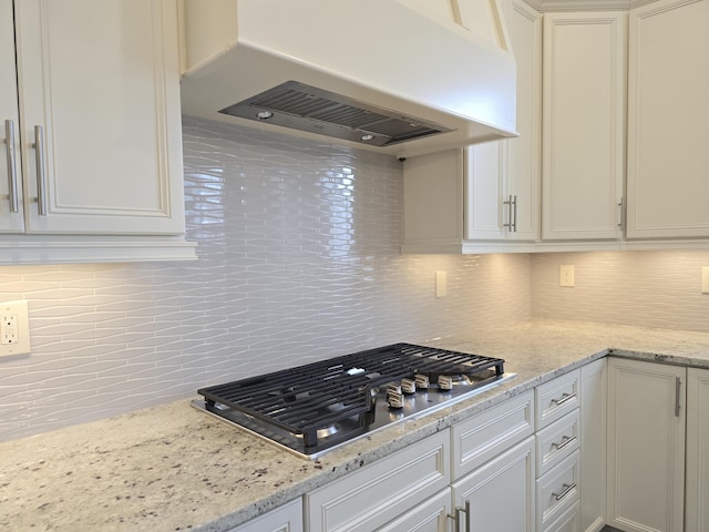 kitchen featuring stainless steel gas cooktop, tasteful backsplash, light stone counters, and ventilation hood