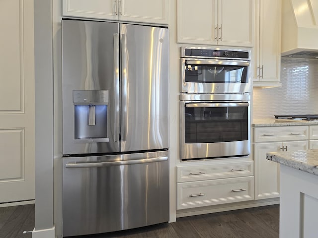 kitchen with white cabinets, backsplash, premium range hood, light stone countertops, and appliances with stainless steel finishes