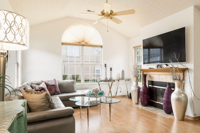 living room featuring light wood-type flooring, a textured ceiling, vaulted ceiling, ceiling fan, and a fireplace