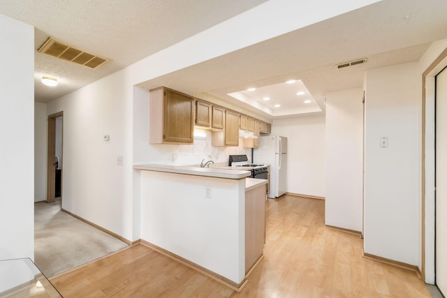 kitchen featuring white refrigerator, kitchen peninsula, range with gas stovetop, a tray ceiling, and light wood-type flooring