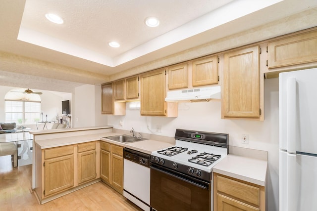 kitchen with kitchen peninsula, white appliances, a tray ceiling, sink, and light hardwood / wood-style flooring