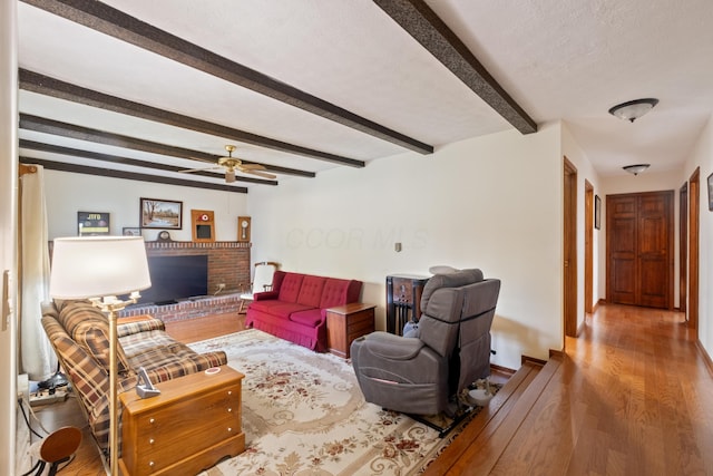 living room featuring a fireplace, a textured ceiling, ceiling fan, beamed ceiling, and hardwood / wood-style floors