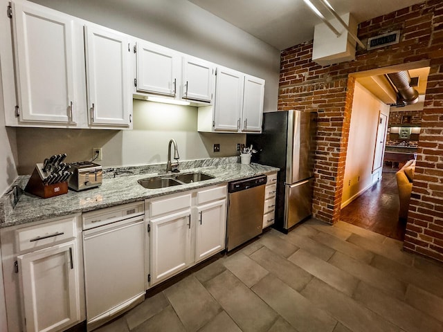 kitchen with appliances with stainless steel finishes, dark hardwood / wood-style flooring, brick wall, sink, and white cabinetry